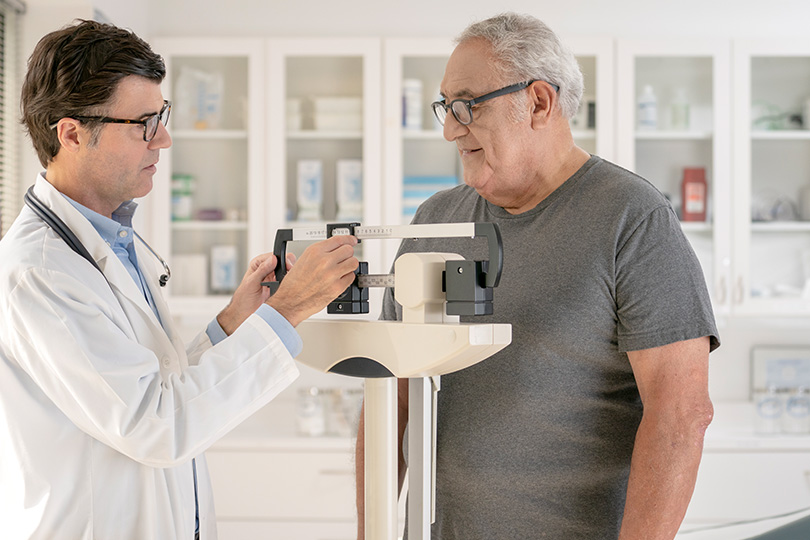 The elderly person is having their weight and BMI checked.