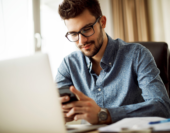 Young man checking email on mobile phone at home.