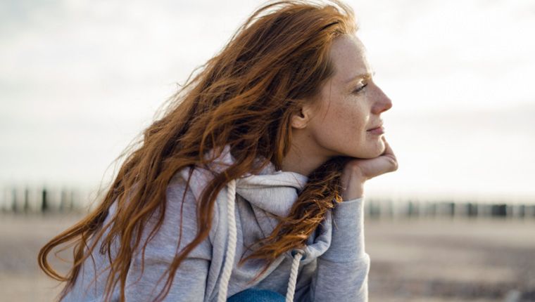 Woman on beach gazes out at water.